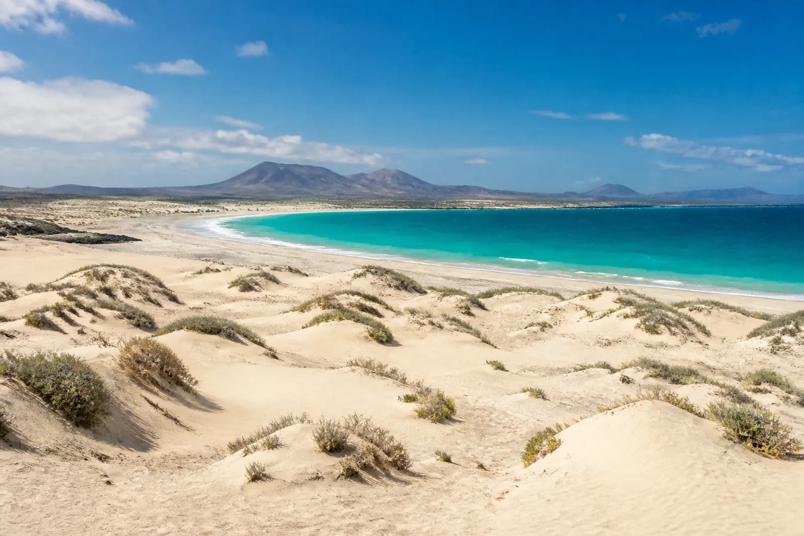 Fuerteventura dunes and turquoise Atlantic water below volcanic hills