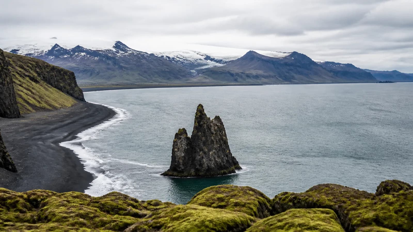 Iceland south coast black sand beach and sea stacks below glacier mountains