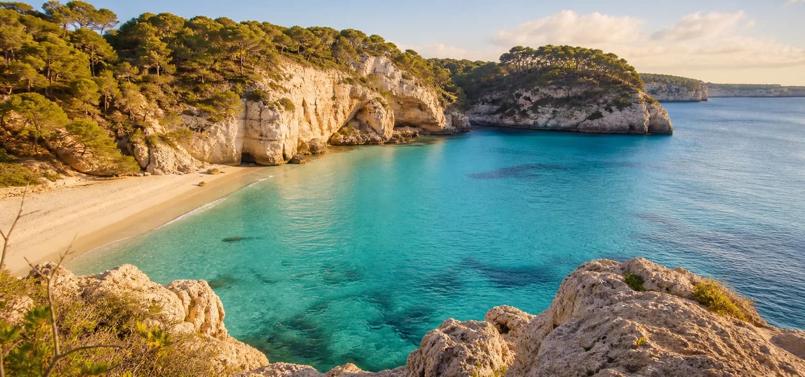 A turquoise Menorca cove framed by limestone cliffs and Mediterranean pines